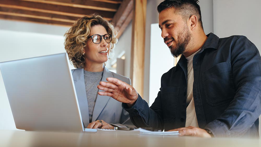 Amtivo (Formerly Certification Europe and EQA) - ISO Standard Certification Transfer - Two people on a laptop discussing what is displayed on the screen. One is explaining what is on the screen to the other.