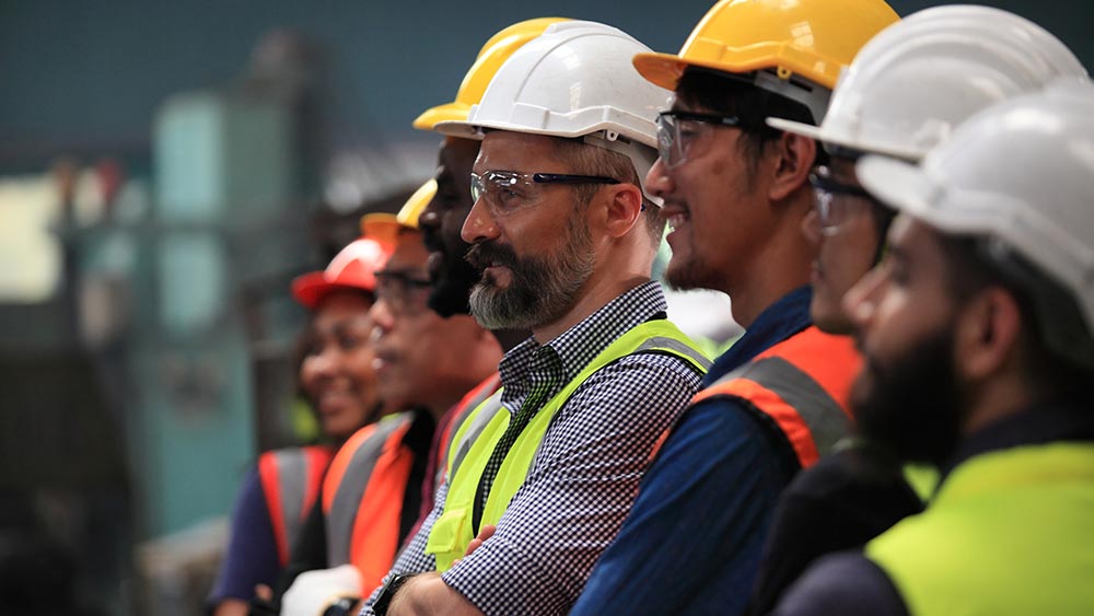 Amtivo (Formerly Certification Europe and EQA) - ISO Certification Transfer - Workers in high visibility jackets and hardhats listening to someone speaking.