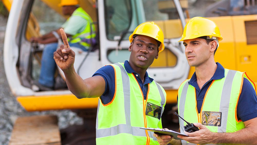 Amtivo (Formerly Certification Europe and EQA) - ISO Certification Transfer - Two construction workers in high visibility jackets and hardhats. One worker pointing and the other holding a clipboard.