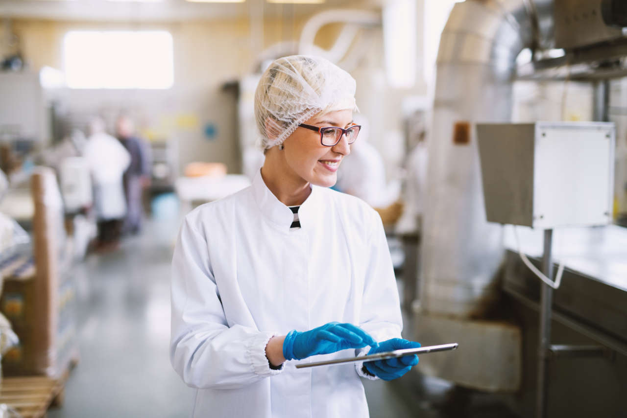 Smiley female worker in sterile clothes using tablet and checking